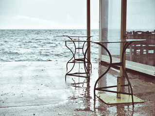 Two tables left on seafront dock during stormy weather. Of season concept.