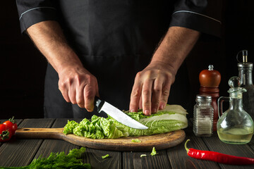 The chef cuts Peking cabbage with a knife. Cooking vegetable salad in a restaurant kitchen