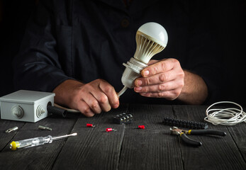 Professional electrician connects the light bulb. Close-up of working hands at work table in workshop during work.