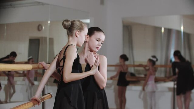Two little girls whispering something to each other near the stand of ballet studio