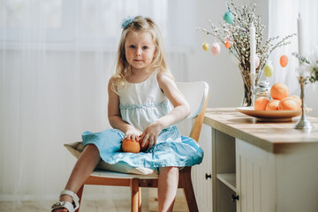 Obraz premium Preparation for the Easter holiday. A little girl is sitting on a chair in a room with fruits in her hands in anticipation of the holiday.