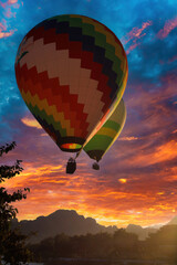 Vang Vieng, Laos - December 15. 2017: View on two colorful hot air balloons over tropical valley against red bright clouds at sunset (focus on balloon in front)