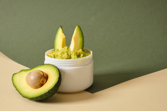 avocado half and white mockup blank jar with avocado puree on wooden stand, green background