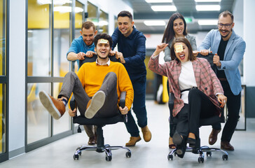 Young cheerful business people  having fun while racing on office chairs and smiling. Friendly work...