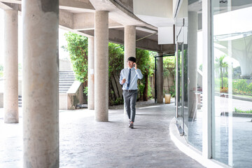 Young business man holding coffee cup and talking on smartphone while walking in office