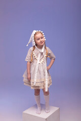 A little beautiful and sweet girl in a stylishly festive dress and with a dwarf hat in a white interior. Photo with selective focus and tinting.The child smiles and looks at the camera.
