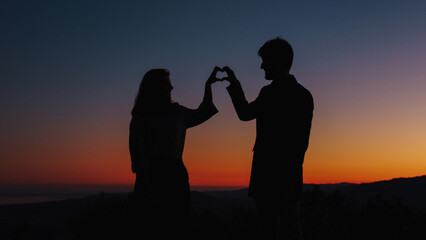Fototapeta na wymiar Silhouette of boy and girl in love make heart symbol 