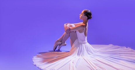 Fototapeta na wymiar an elegant ballerina in pointe shoes sits stretching her legs in a long white skirt on a lilac light background