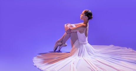 an elegant ballerina in pointe shoes sits stretching her legs in a long white skirt on a lilac...