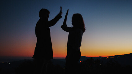 Fototapeta na wymiar Silhouette of boy and girl high five at sunset