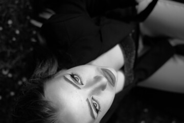 Black and white portrait of a young girl in the city park. Elegant and melancholy portrait, the girl is sitting on the grass. Beautiful woman in classic clothes