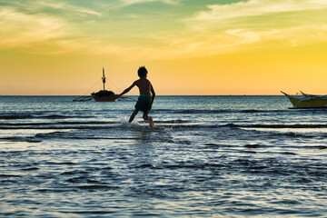 Sunset water play. Silhouette of a boy on a waterboard. Bulalaco, Oriental Mindoro, the Philippines, 