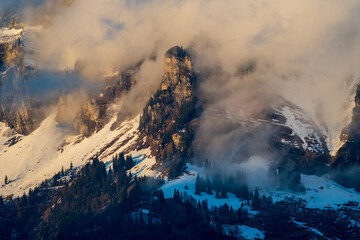 Bergkette von Wolken umgeben wird von der Sonne angeschienen. Ein nebulöses, eindrückliches Bild.