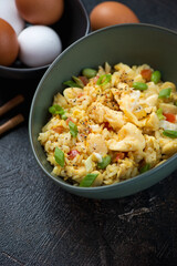 Bowl of chinese fried rice mixed with scrambled eggs, middle close-up on a dark-brown stone surface, vertical shot