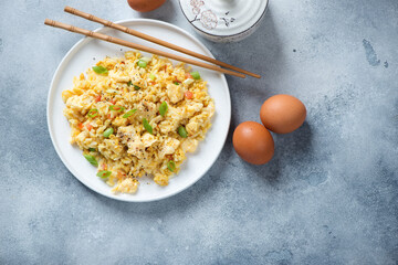 White plate with chinese egg fried rice on a light-blue stone background, flat lay, horizontal shot with space