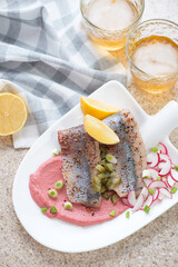 White shovel-shaped plate with herring fillet and beetroot mousse, vertical shot on a beige marble surface, elevated view