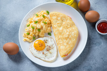 White plate with chicken eggs cooked in different ways, elevated view on a light-blue stone background, studio shot