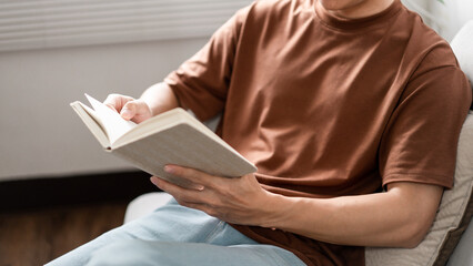 Technology Concept The male with his glasses sitting on the grey sofa, leaning his back on it, and reading a book