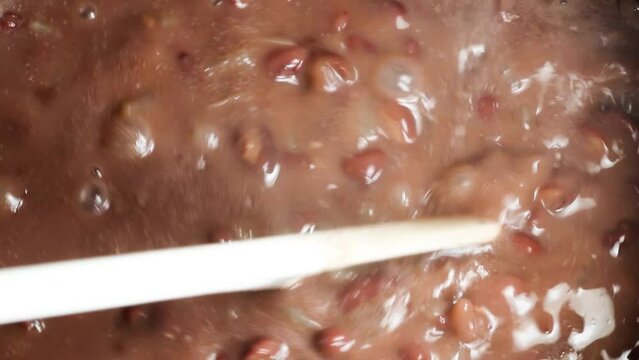 Stirring with the spoon in red beans cooking in the stone pot.