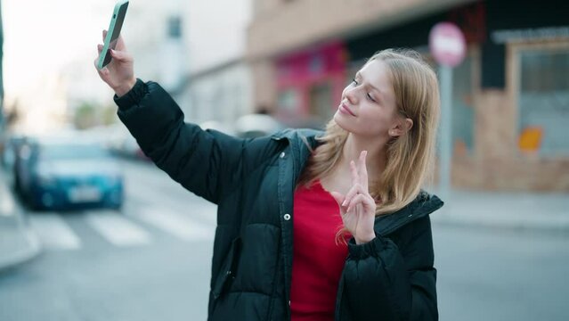 Young blonde girl smiling confident making selfie by the smartphone at street