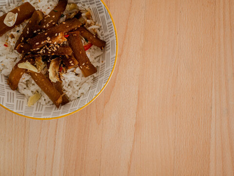 Off center top-view of a vegetarian teriyaki and rice bowl on a wood table