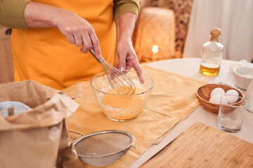 Obraz na płótnie Canvas Caucasian elderly woman mixing ingredients with whisk into the bowl while cooking at the kitchen