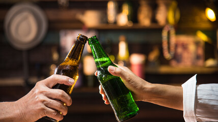 two hands hold beer bottle toasting in bar - obrazy, fototapety, plakaty
