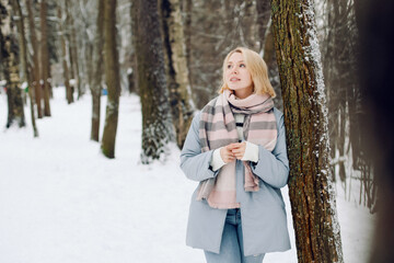 Beautiful young blond women in warm blue coat in winter park smile. Outdoor photo.