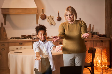 Grandmother and granddaughter making different similar poses in front of the tablet computer