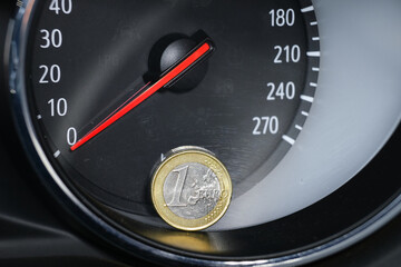 Close up of a one euro coin in front of an analog speedometer. Money in front of a speed indicator....