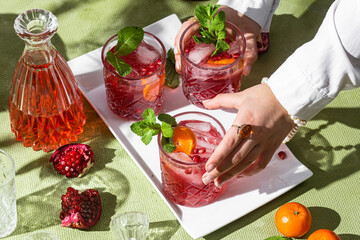 Cocktail with pomegranate juice and ice in a glass on a light green background