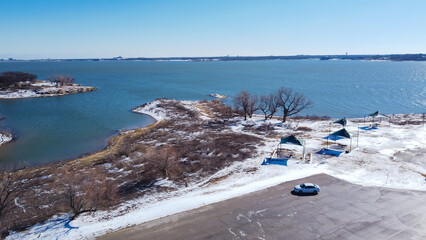 Top view snow covered lakeside tent and pavilion along shoreline with nearby parking at Murrell...