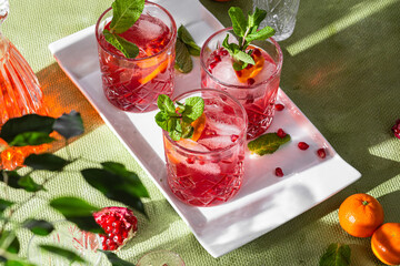Cocktail with pomegranate juice and ice in a glass on a light green background