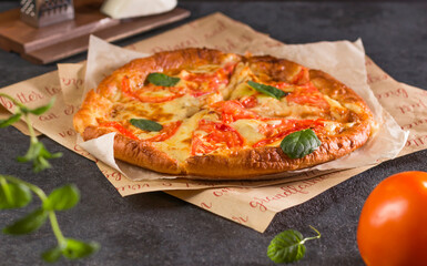 Delicious fresh and homemade fast food. Traditional pizza Margherita with tomatoes, basil and mozzarella cheese close-up parchment paper on a dark background