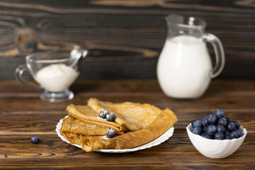 Pancakes Thin homemade pancakes with berries, with a jug of milk and sour cream on a wooden table. traditional Russian cuisine. Selective focus.