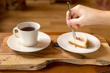 A young woman is eating cheesecake and drinking tea, a close-up of a female hand using a fork to take a piece of cake.