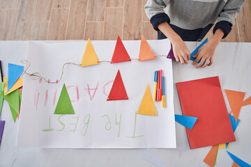 Caucasian child standing at the table and preparing holiday decor and placard for the Fathers day