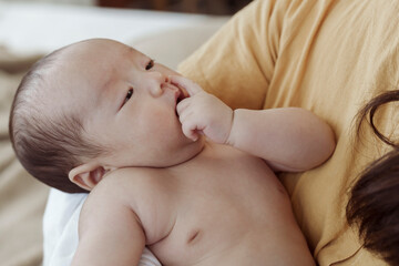 Close-up of a 2-month-old Asian newborn boy, undressed on his mother's lap. There is a mother who takes care of closely
