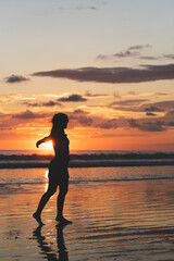 Fototapeta premium vertical portrait, Silhouette of a woman with open arms enjoying a sunset on a beach in Costa Rica.