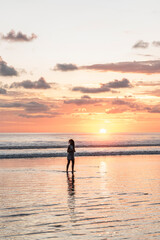 Fototapeta premium vertical portrait, Silhouette of a woman enjoying a sunset on a beach in Costa Rica.