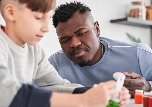Curious multiracial father watching how his caucasian son coloring eggs for Easter