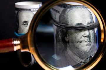 Rolls of USD banknotes under a magnifying glass on a black background 