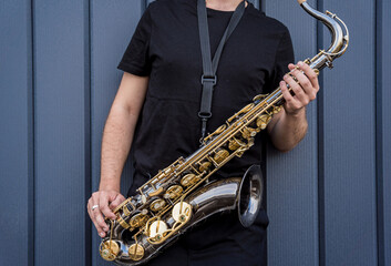 Naklejka premium Young street musician playing saxophone near the big blue wall
