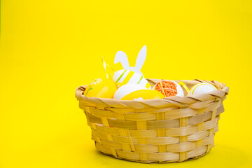 Fototapeta premium Colorful Easter eggs in a wicker basket and a wooden box on a yellow, green background. Space for text
