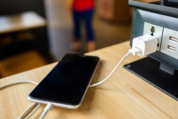 Closeup USB port and adapter at the electrical power socket on the table, phone during charging in...