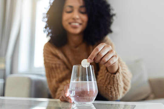 Closeup of a young woman dropping an effervescent antacid in a glass of water. young woman hardly put a soluble pill with a medicine for pain or a hangover in a glass of water