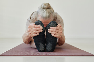 Senior active female holding her feet while bending forwards and keeping head on stretched legs...