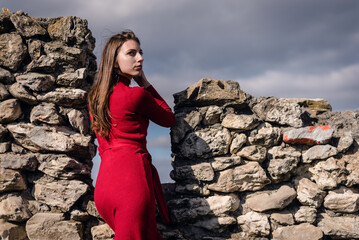 Young girl in the red dress stands among the ancient ruins.