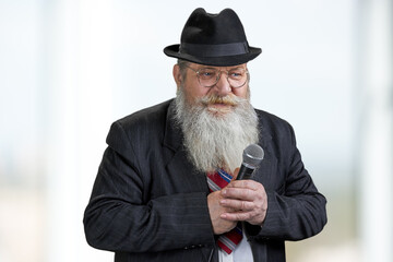 Confident senior man with beard holding microphone on blurred background.