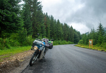 Fototapeta na wymiar Asphalt empty road in coniferous mountains, traveler's bike moped by roadside, freedom and journey concept
